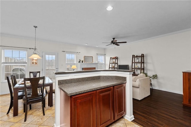 kitchen with reddish brown cabinets, baseboards, dark countertops, a center island, and decorative light fixtures