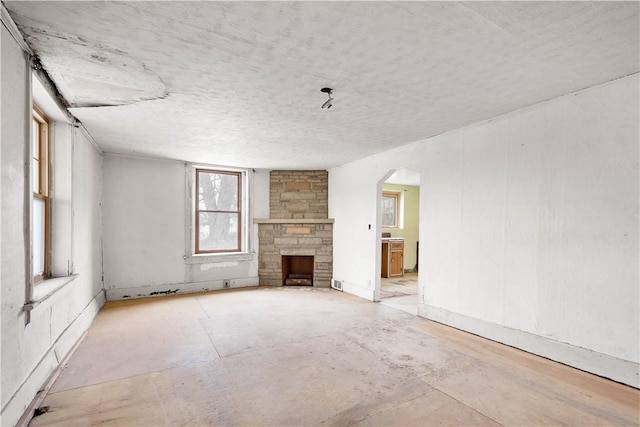 unfurnished living room featuring arched walkways and a stone fireplace