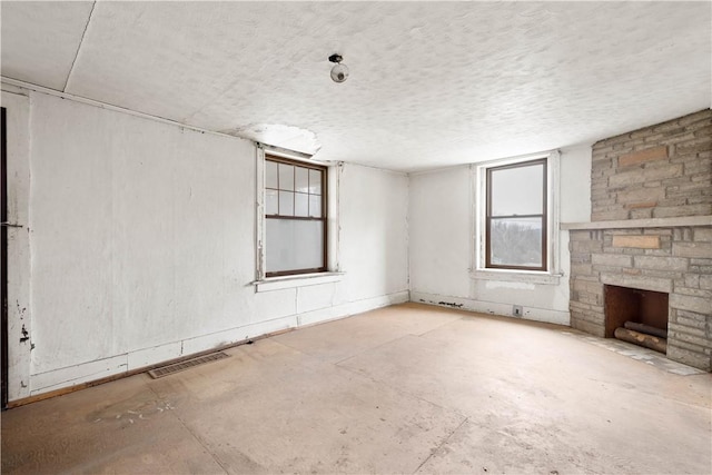 unfurnished living room with a fireplace, visible vents, a textured ceiling, and unfinished concrete floors