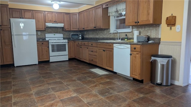 kitchen with dark countertops, wainscoting, a sink, white appliances, and under cabinet range hood