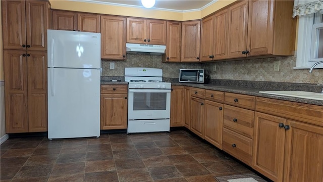 kitchen featuring white appliances, tasteful backsplash, dark countertops, under cabinet range hood, and a sink