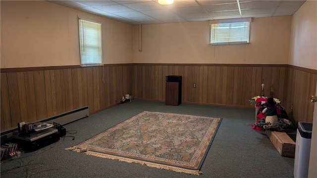 below grade area featuring light carpet, a wainscoted wall, a drop ceiling, and wood walls