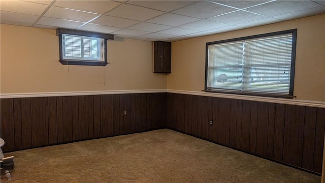 basement with a paneled ceiling, wood walls, carpet, and a wainscoted wall