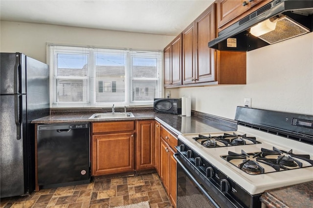 kitchen featuring brown cabinets, stone finish flooring, a sink, under cabinet range hood, and black appliances