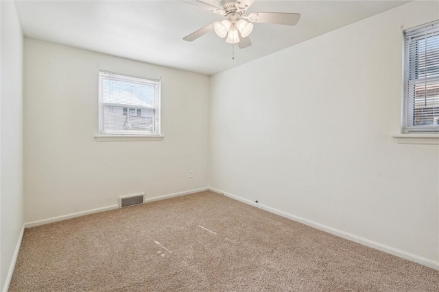 carpeted spare room featuring a ceiling fan, visible vents, and baseboards