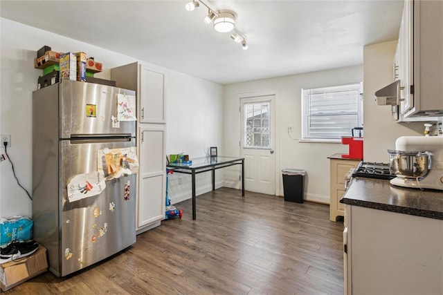 kitchen featuring freestanding refrigerator, wall chimney range hood, dark countertops, and wood finished floors