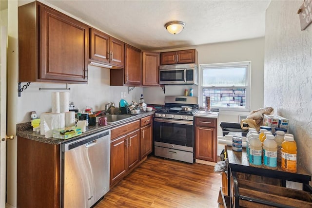 kitchen with dark wood-style floors, stainless steel appliances, a sink, and brown cabinetry