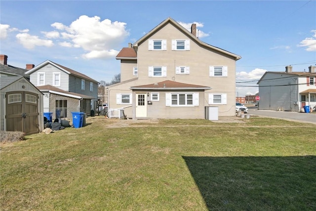 rear view of property with a storage shed, a chimney, a lawn, and an outbuilding