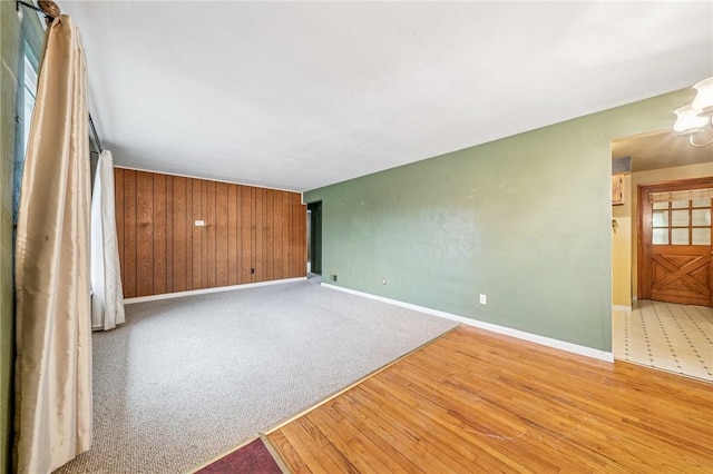 empty room with carpet flooring, wooden walls, baseboards, and wood finished floors