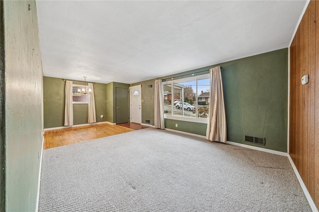 empty room featuring carpet floors, visible vents, a notable chandelier, and baseboards