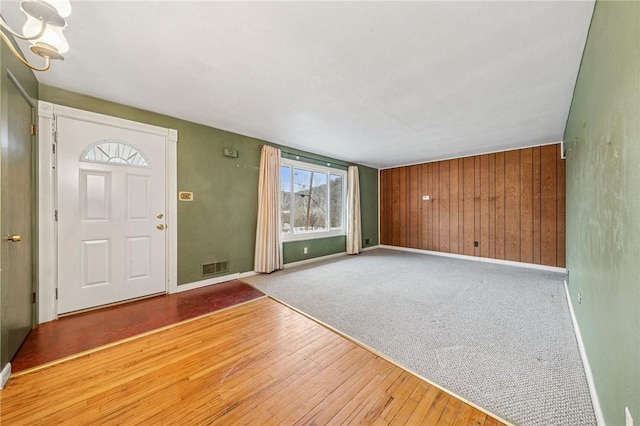 foyer featuring visible vents, carpet flooring, wood walls, wood finished floors, and baseboards