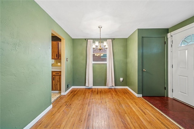 unfurnished dining area featuring a notable chandelier, light wood finished floors, visible vents, a textured wall, and baseboards