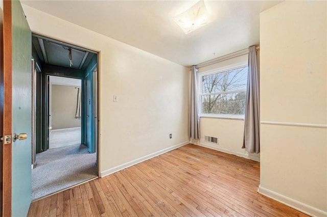 unfurnished room featuring baseboards, light wood-style flooring, visible vents, and attic access