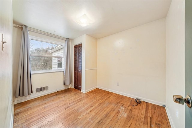 empty room with hardwood / wood-style flooring, baseboards, and visible vents