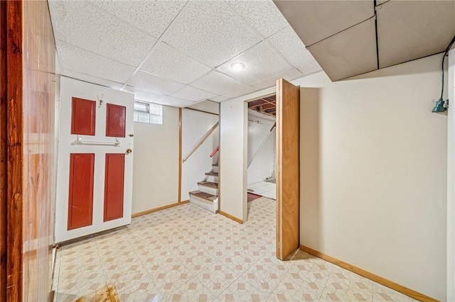 basement featuring stairs, a paneled ceiling, baseboards, and tile patterned floors