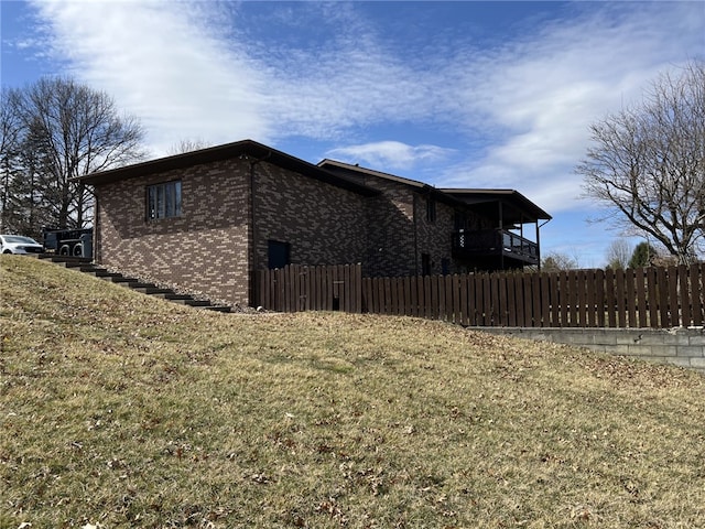 view of property exterior with a yard, brick siding, fence, and a balcony