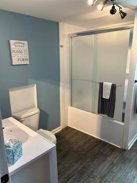 bathroom featuring toilet, bath / shower combo with glass door, wood finished floors, and vanity