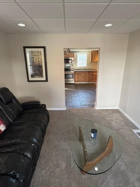 living area featuring a paneled ceiling and baseboards