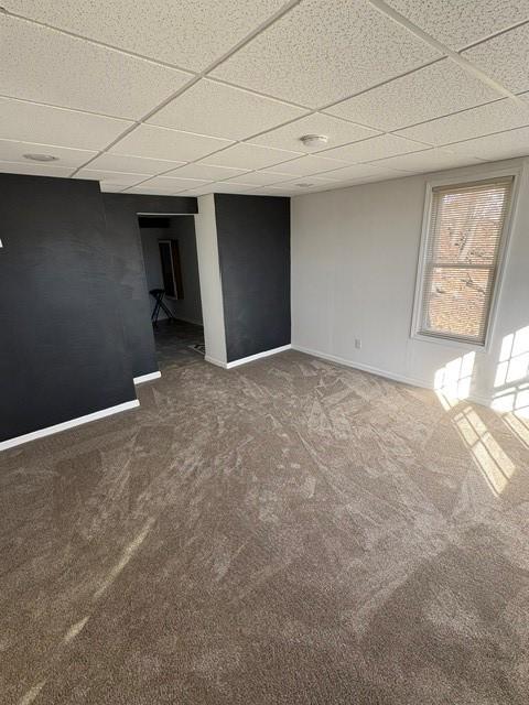 carpeted empty room with a paneled ceiling and baseboards