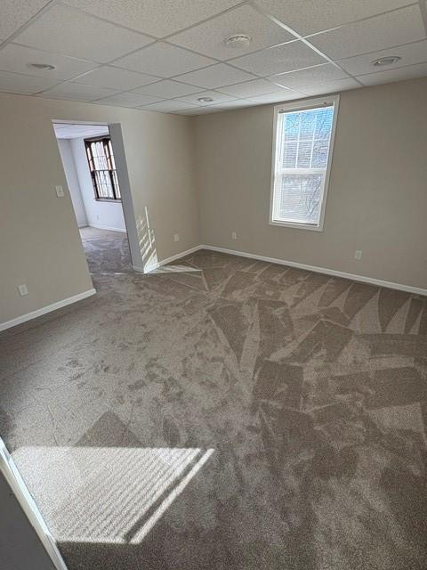 carpeted empty room featuring a drop ceiling, plenty of natural light, and baseboards