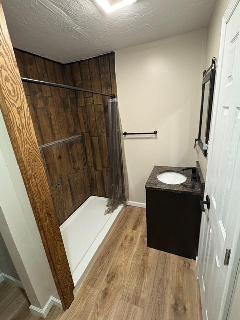 bathroom with a stall shower, vanity, a textured ceiling, wood finished floors, and baseboards