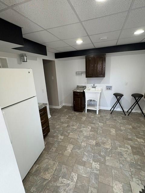 kitchen with a paneled ceiling, freestanding refrigerator, a sink, dark brown cabinetry, and baseboards