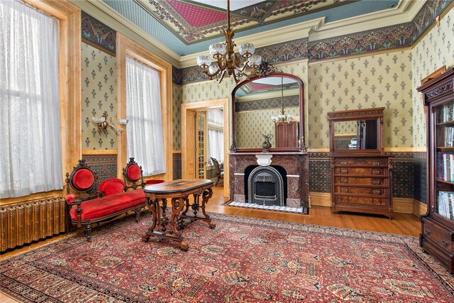 sitting room featuring wallpapered walls, radiator, a wainscoted wall, crown molding, and a notable chandelier