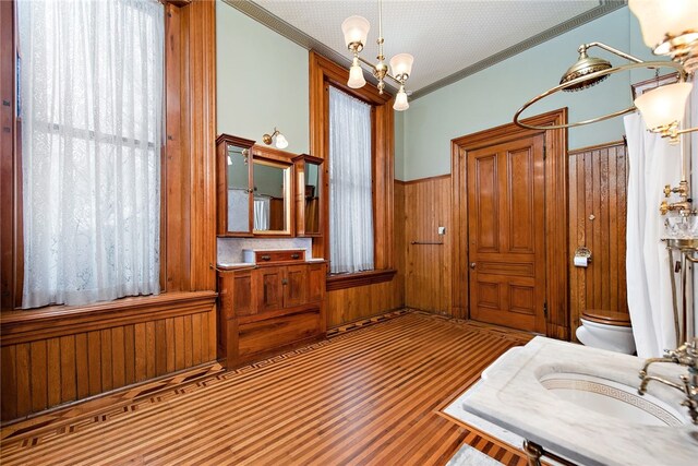 full bath with wooden walls, toilet, a wainscoted wall, an inviting chandelier, and crown molding