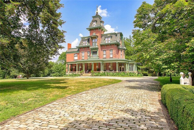 view of front of house featuring a porch, decorative driveway, a front lawn, and mansard roof