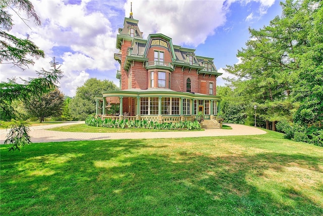 rear view of house featuring covered porch, brick siding, a lawn, and mansard roof