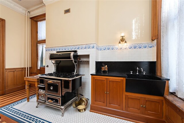 kitchen featuring a wainscoted wall, dark countertops, visible vents, brown cabinetry, and a sink