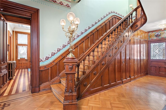 stairway featuring a healthy amount of sunlight, wood walls, a notable chandelier, and radiator heating unit