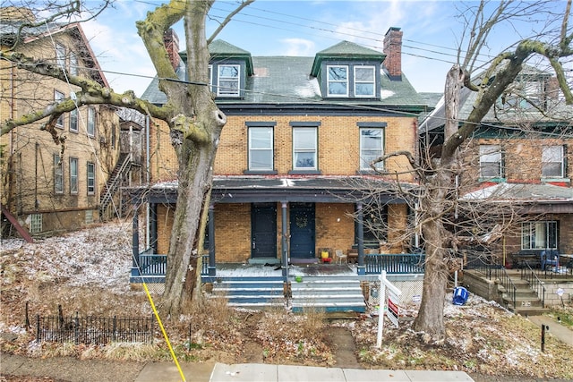 view of front facade with a porch, brick siding, and a chimney