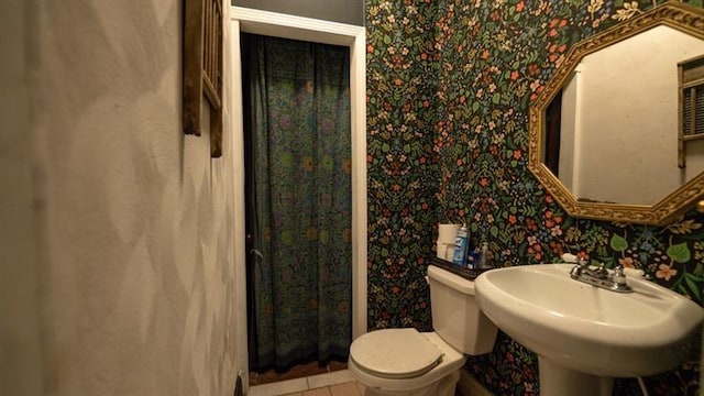 half bathroom with wallpapered walls, a sink, toilet, and tile patterned floors