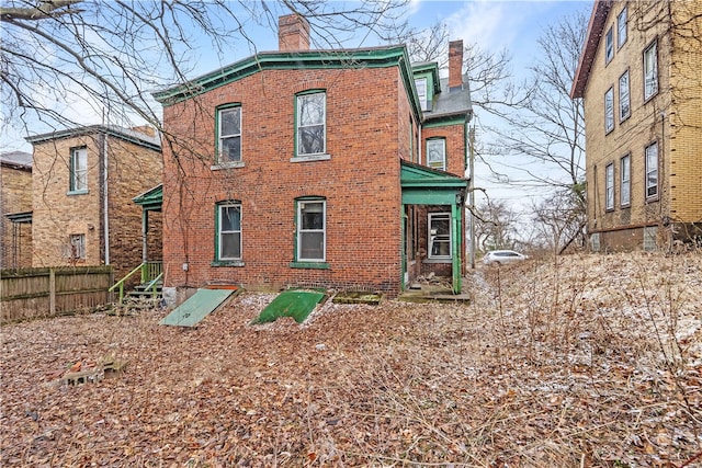 rear view of house featuring brick siding, a chimney, and fence