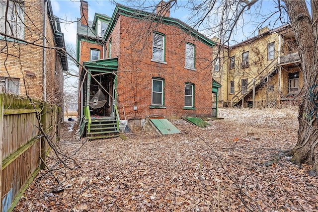 back of house with brick siding, fence, and a chimney