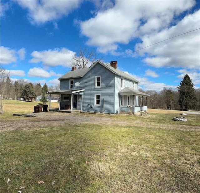 back of house with driveway, a porch, a chimney, and a lawn