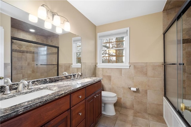 full bath featuring tiled shower, a sink, tile walls, and toilet