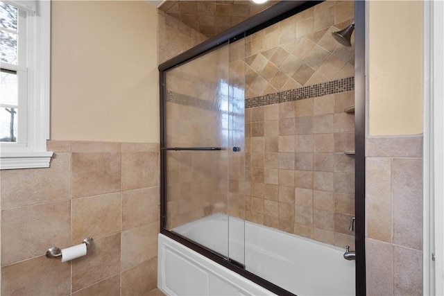 bathroom with combined bath / shower with glass door, tile walls, and wainscoting