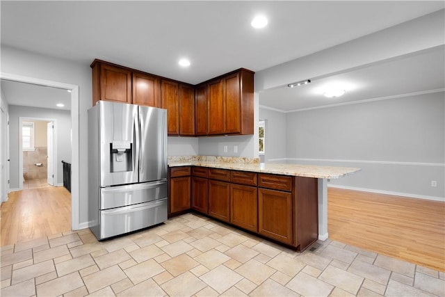 kitchen featuring a peninsula, stainless steel refrigerator with ice dispenser, light stone countertops, and a healthy amount of sunlight