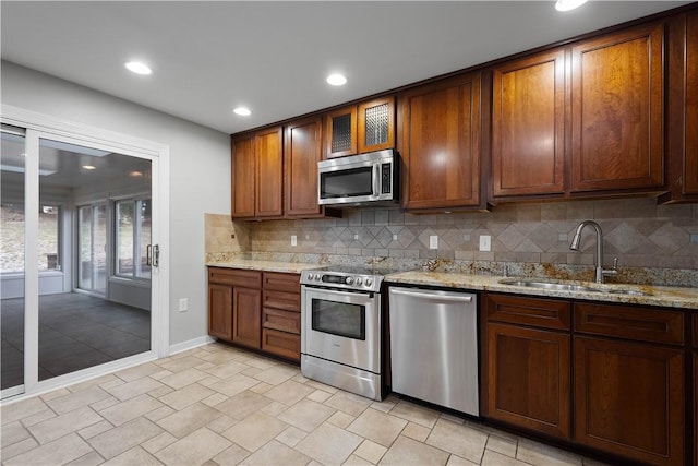 kitchen featuring stainless steel appliances, light stone countertops, a sink, and tasteful backsplash