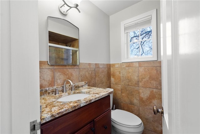 bathroom featuring toilet, a wainscoted wall, vanity, a shower stall, and tile walls