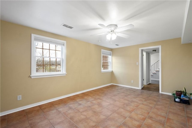 tiled empty room with a ceiling fan, plenty of natural light, visible vents, and baseboards