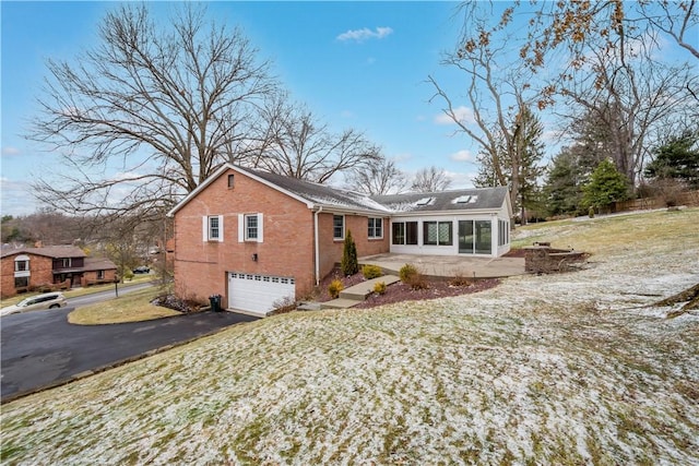 view of front of home featuring a garage, driveway, brick siding, and a sunroom