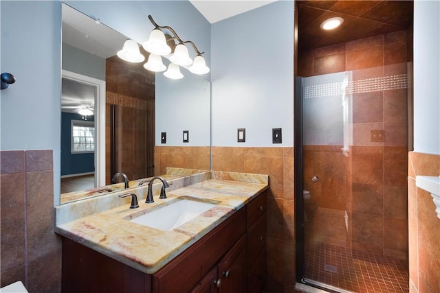 bathroom with wainscoting, toilet, vanity, tile walls, and ceiling fan with notable chandelier