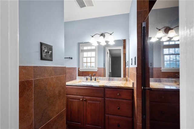 bathroom with visible vents, a wealth of natural light, wainscoting, and tile walls