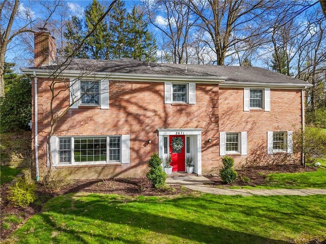 colonial house featuring a chimney, brick siding, and a front yard