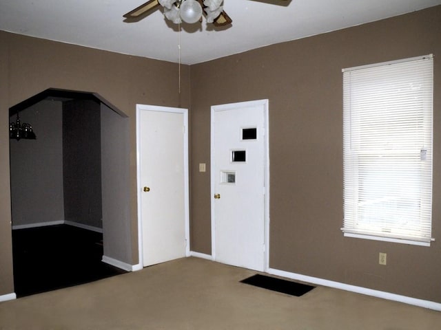 unfurnished bedroom featuring arched walkways, carpet flooring, a ceiling fan, and baseboards