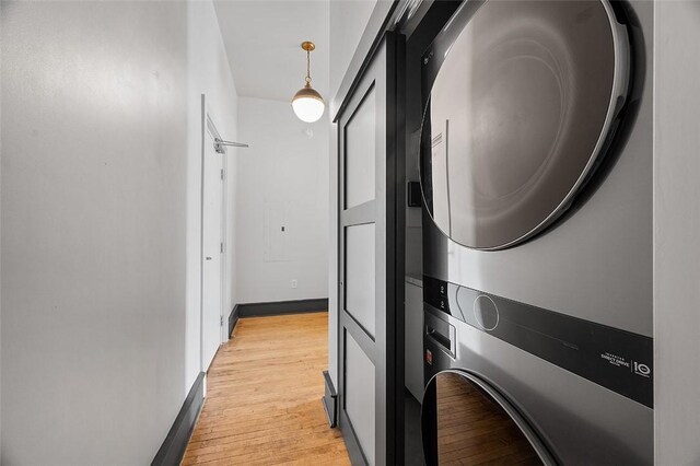 laundry room featuring laundry area, light wood-type flooring, stacked washer and clothes dryer, and baseboards