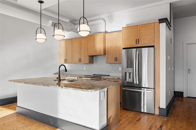 kitchen with stone counters, stainless steel appliances, a sink, decorative backsplash, and hardwood / wood-style floors